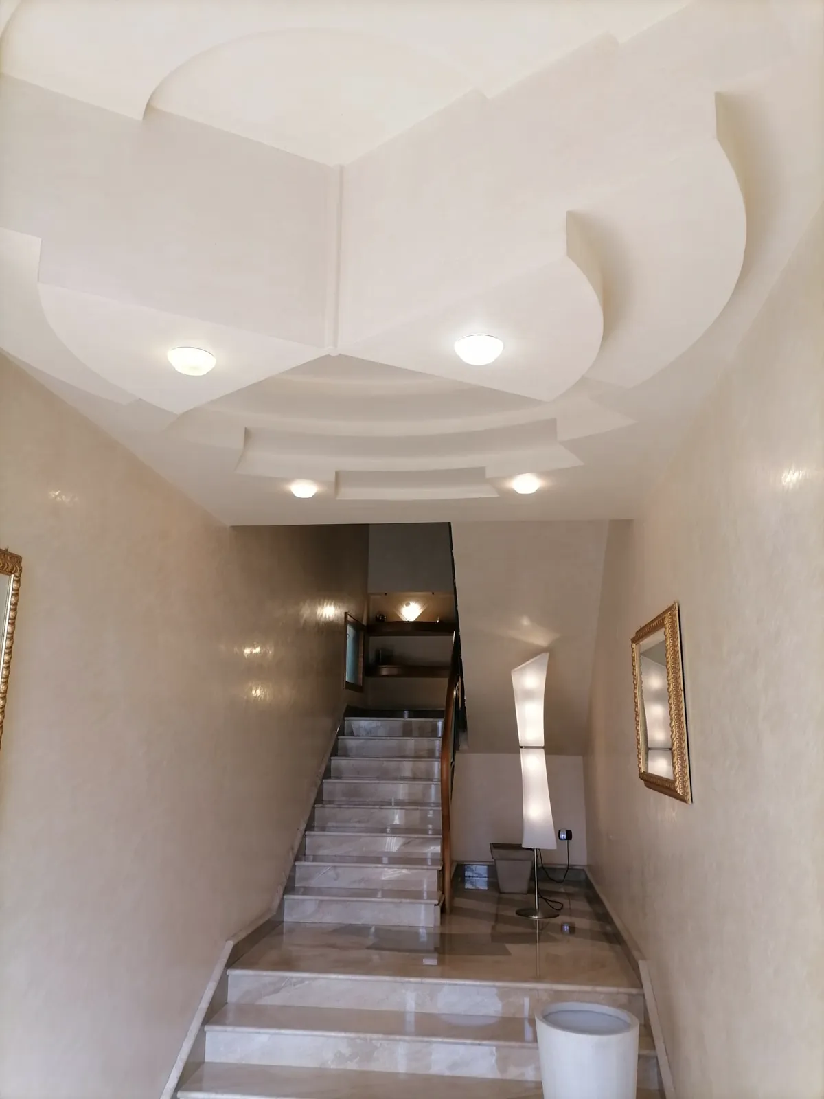Ingresso con controsoffitto in cartongesso sagomato, faretti incassati e pareti a stucco lucido, scala sullo sfondo